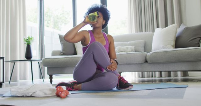 Happy african american wearing sportswear, exercising, drinking water. domestic lifestyle, spending free time at home.