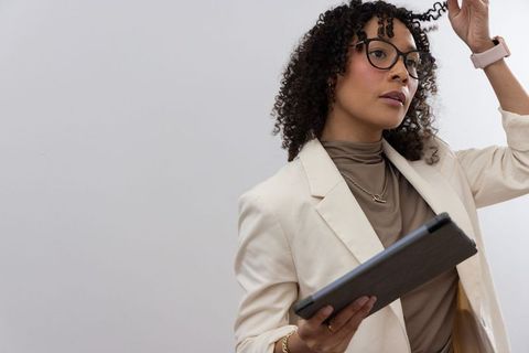African american businesswoman adjusting curl while holding tablet in blazer and glasses