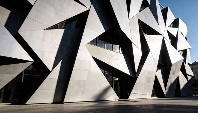 Angular metallic facade casting dramatic geometric shadows at modern urban plaza