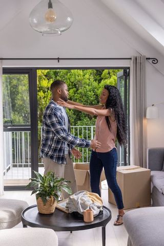 Couple reaching for embrace while unpacking in modern bright living room with balcony