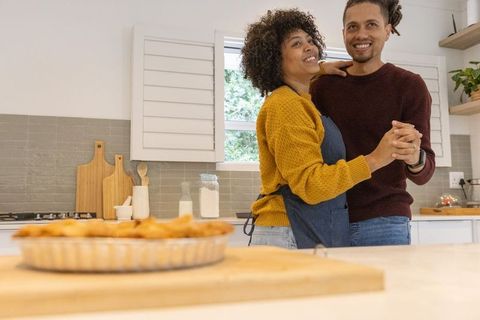 Couple dancing in sunlit kitchen baking pie, warm home romance and comfort
