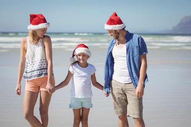 Family enjoying a sunny day at the beach while wearing Santa hats. Perfect for holiday-themed promotions, travel advertisements, and festive greeting cards. Highlights the joy of spending holidays together in a tropical setting.