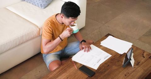 Young Man Reviewing Documents Beside Coffee Table at Home