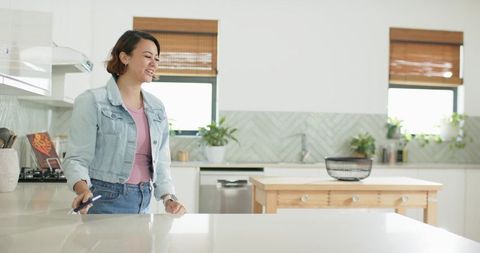 African american woman smiling using smartphone at sleek kitchen island in modern home