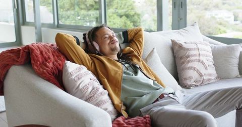 Relaxed man reclining on sofa listening to music with headphones in sunlit living room