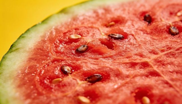 Close-up watermelon slice shining with juicy red flesh and seeds on yellow background
