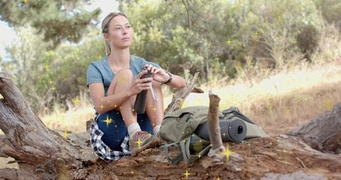 Young woman resting on fallen log with backpack and water bottle in sunlit forest