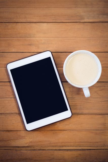 Overhead view of digital tablet with coffee cup on wooden table