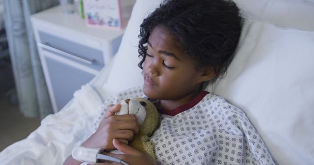 Biracial girl lying on hospital bed wearing fingertip pulse oximeter and holding teddy bear. medicine, health and healthcare services.