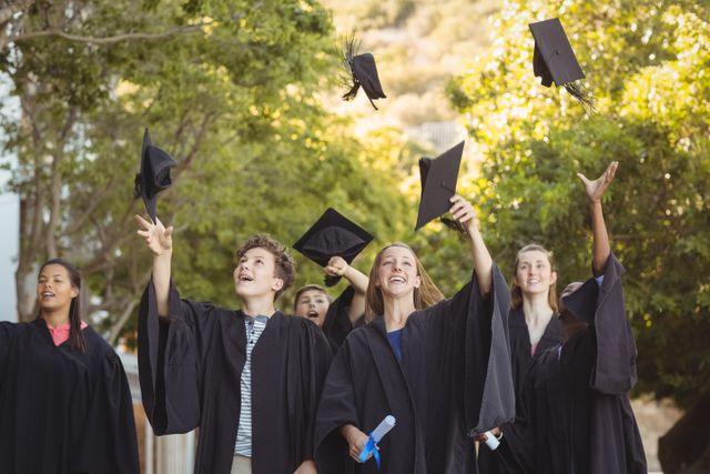 Group of students celebrating graduation by throwing their mortarboards in the air. Ideal for use in educational materials, school brochures, graduation announcements, and articles about academic success and student life.
