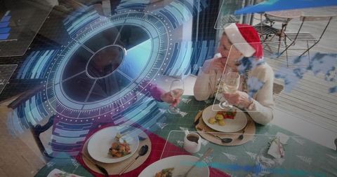 Senior couple wearing santa hats toasting wine on deck with festive hud overlay