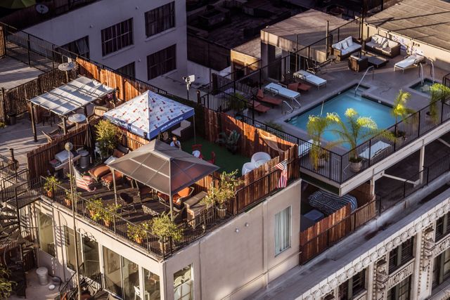 High-angle view of rooftop patio and swimming pool in an urban setting with outdoor furniture and plants. Ideal for use in lifestyle blogs, urban planning articles, architecture features, and real estate marketing. Showcases a modern and relaxed urban residential space.