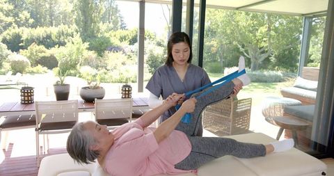 Senior woman receives physiotherapy assistance for leg exercises at home