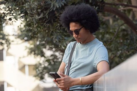 African american man leaning on concrete railing checking smartphone in urban green space