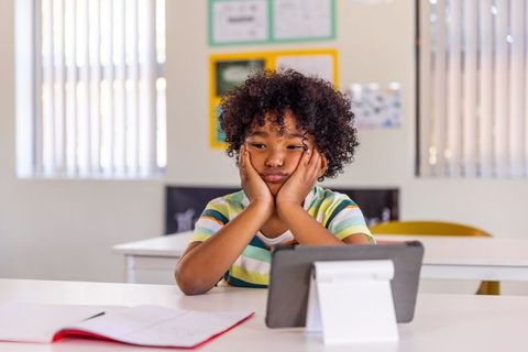 African american schoolboy looking bored while using tablet for remote learning