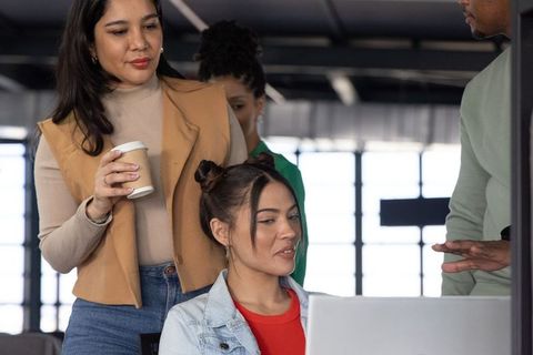 Diverse team collaborating around laptop in modern coworking space with coffee and daylight