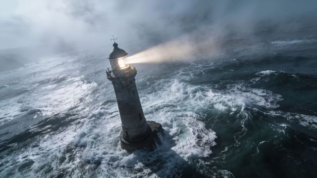 Solitary lighthouse beaming through stormy seas, crashing waves surrounding rocky islet