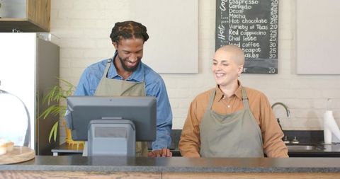 Smiling diverse baristas operating touchscreen pos behind rustic cafe counter