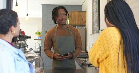 African american barista serving customers with tablet at cafe counter, coffee service