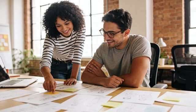 Young design duo collaborating over sketches and sticky notes in bright loft studio