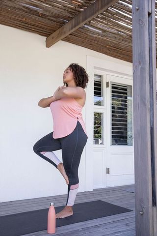 Woman practicing tree pose under pergola with water bottle