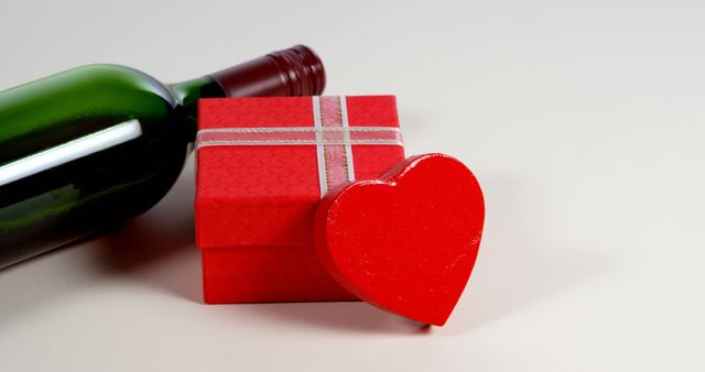 A bottle of wine lies next to a red gift box with a heart-shaped tag, suggesting a romantic occasion, with copy space. The items evoke themes of celebration, love, or a special event such as an anniversary or Valentine's Day.