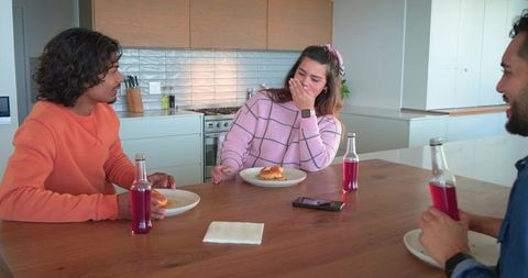 Three friends laughing and sharing sandwiches at modern bright kitchen island