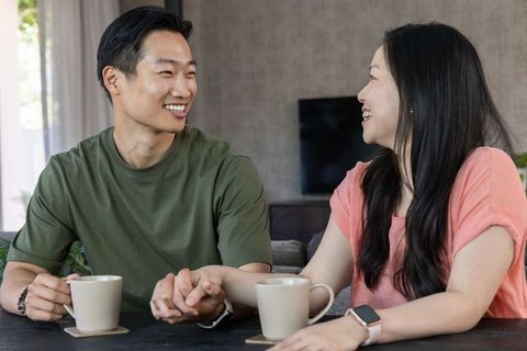 Asian couple holding hands and smiling over coffee in cozy living room bright intimate moment