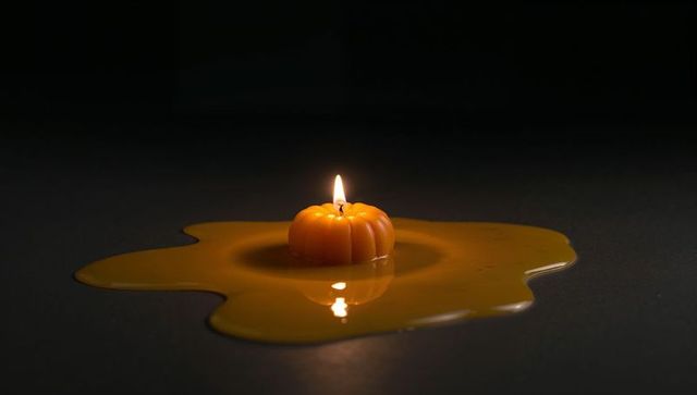 Pumpkin Candle Melting with Warm Reflections on Dark Surface
