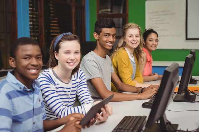 Diverse group of students sitting in a computer classroom, smiling and engaging with technology. Ideal for educational websites, school brochures, and articles about modern education, teamwork, and digital learning.