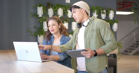 Young diverse coworkers collaborating at wooden counter using laptop and tablet