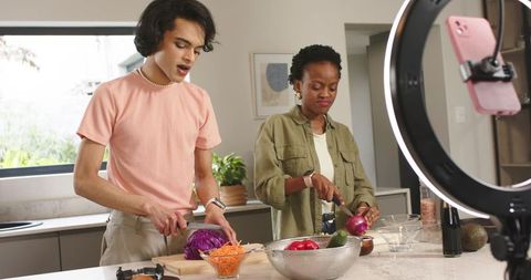 Young creators cooking together at kitchen island recording vlog with ring light phone