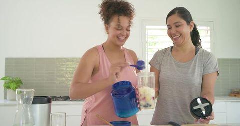 Multiracial friends preparing protein smoothie, scooping supplement into blender bottle