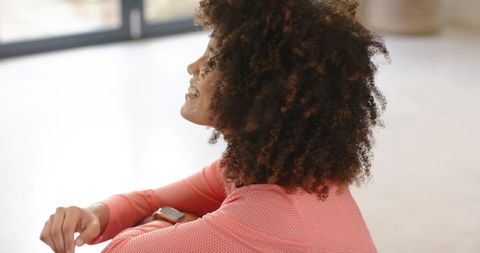 Young woman relaxing in coral top with smartwatch and natural curls in bright minimalist interior