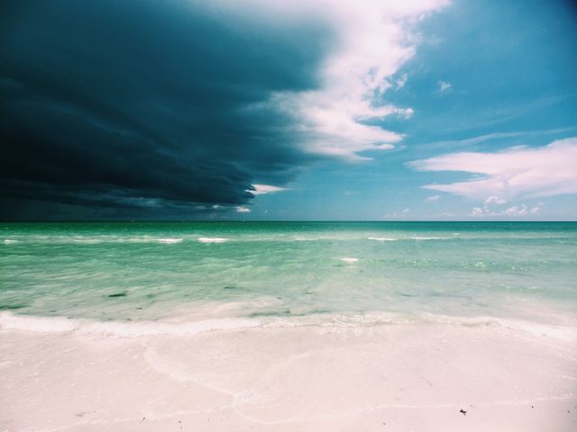 Calm Beach with Encroaching Storm Clouds Over Turquoise Water - Download Free Stock Photos Pikwizard.com