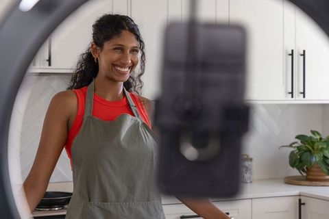 African american woman filming cooking tutorial in modern kitchen with ring light