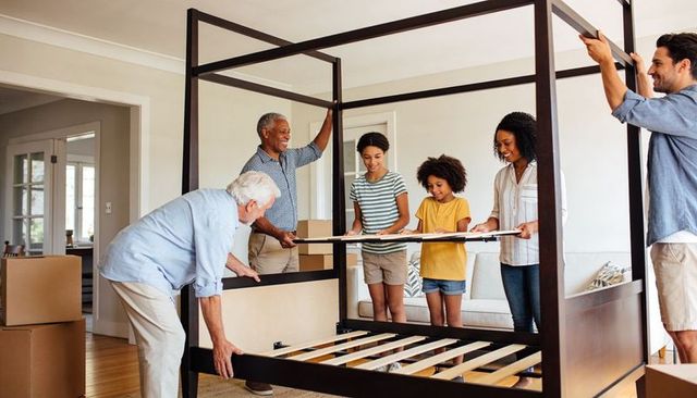 Multigenerational family assembling wood four-poster bed during move in bright living room