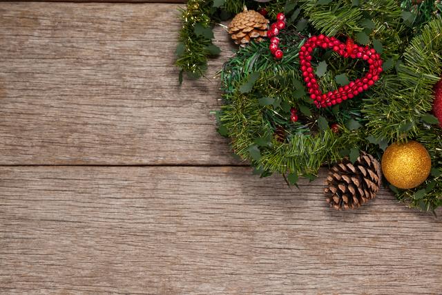 Christmas wreath adorned with pine cones, red heart, and gold ornament on rustic wooden background. Perfect for holiday greeting cards, festive invitations, seasonal advertisements, and home decor inspiration.