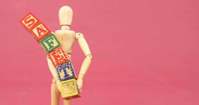 Wooden Mannequin Holding Safety Block Letters Against Pink Background - Download Free Stock Images Pikwizard.com