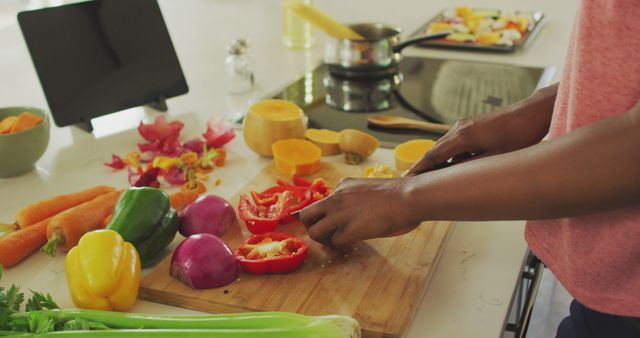 Person cutting various colorful vegetables on a wooden cutting board in a modern kitchen. Display includes bell peppers, carrots, and onions, suggesting a healthy lifestyle and meal preparation. Ideal for use in websites, blogs, and articles focusing on cooking, dietary health, and culinary skills.