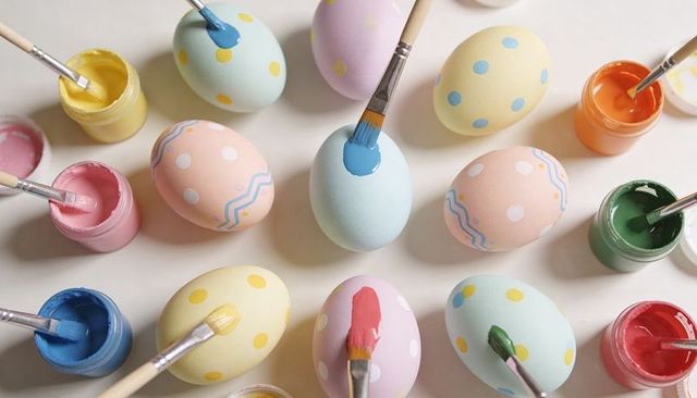 Pastel easter eggs being hand painted with brushes, polka dot designs and open paint jars