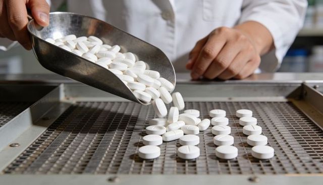 Pharmaceutical tablet manufacturing pouring white tablets from stainless scoop onto metal grid