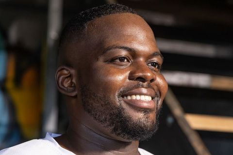 African man smiling and looking right in stairwell, warm-lit closeup portrait headshot