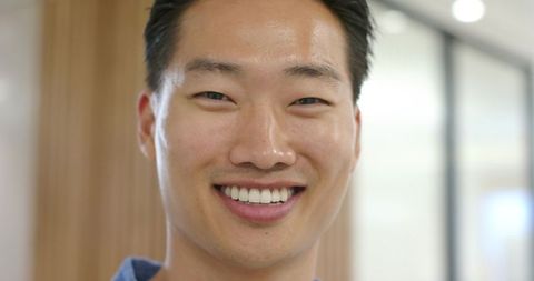 Confident asian man smiling headshot in modern office with glass partition and wood panels