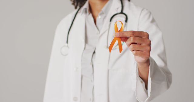Image of smiling biracial female doctor holding orange kidney cancer ribbon. global medicine and healthcare concept.