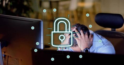 IT worker holding head at workstation with glowing padlock representing data breach stress