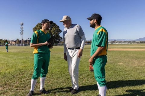 Baseball coach leading dugout strategy talk with two uniformed players on grass field