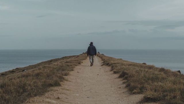 Solitary hiker walking along windswept coastal path toward distant horizon