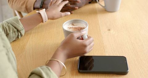 African American friends sharing cozy coffee conversation at wooden table with smartphone