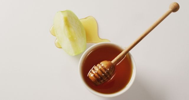 Green apple slice drizzled with honey, placed beside honey pot with dipper. Ideal for use in health food blogs, recipe articles, and advertisements promoting natural sweeteners or organic foods.